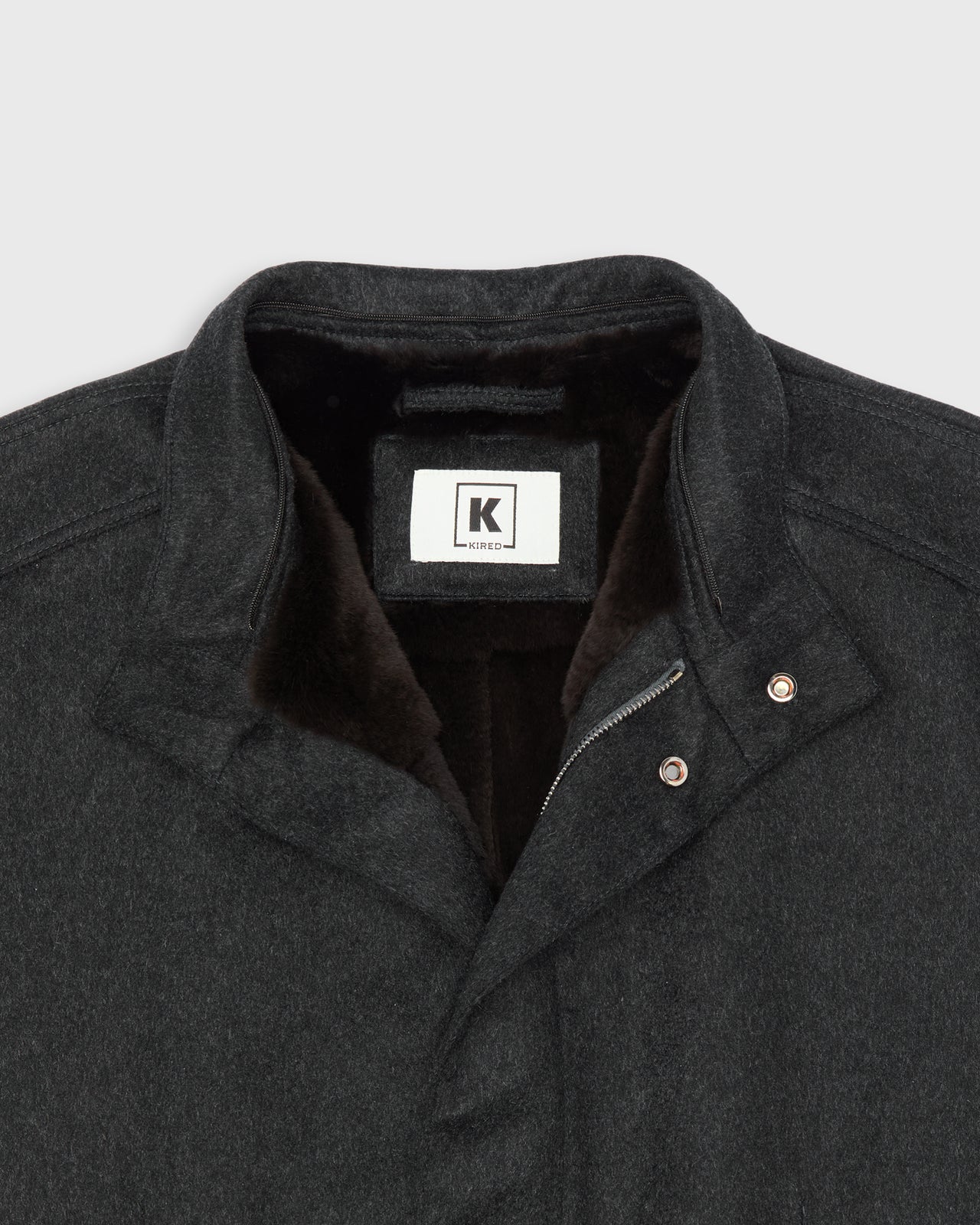 Close-up of a dark charcoal gray cashmere jacket with a brown beaver fur lining, featuring a hanger hook, zipper, and snap closures.